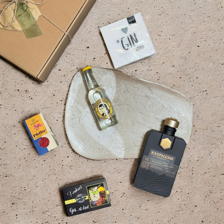 Ausgepacktes Gin Geschenkset mit Kaufmann Spirits Mountain Gin Thomas Henry Tonic Water Fenkart Gin Schokolade Sonnentor Pfeffer rosa ganz bio und ppd Gin Lover Cocktail Servietten