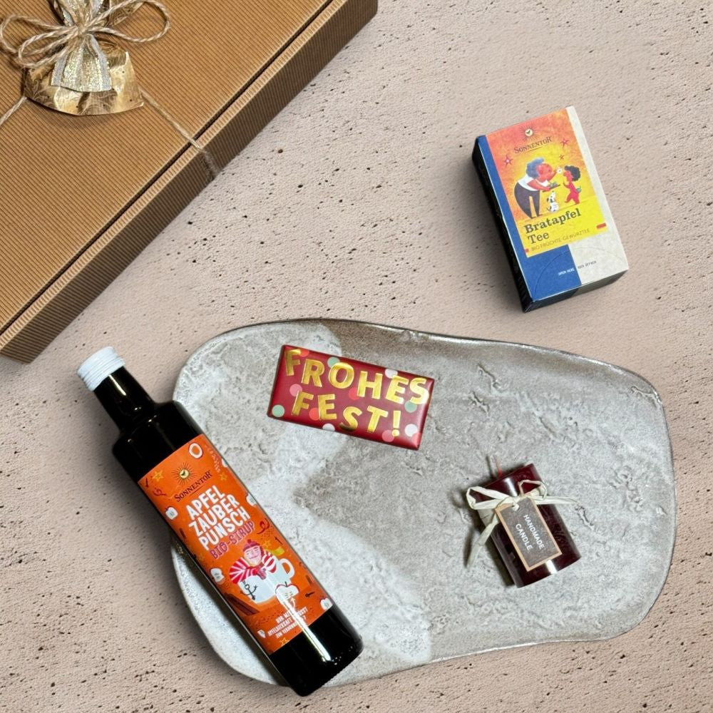 Ausgepacktes Apfel Punsch Geschenkset mit Sonnentor Apfelzauber Punsch Sirup bio 500ml Sonnentor Bratapfel Tee 45g Grafik Werkstatt Schokolade Frohes Fest und Kerze Blending Colors bordeaux mix
