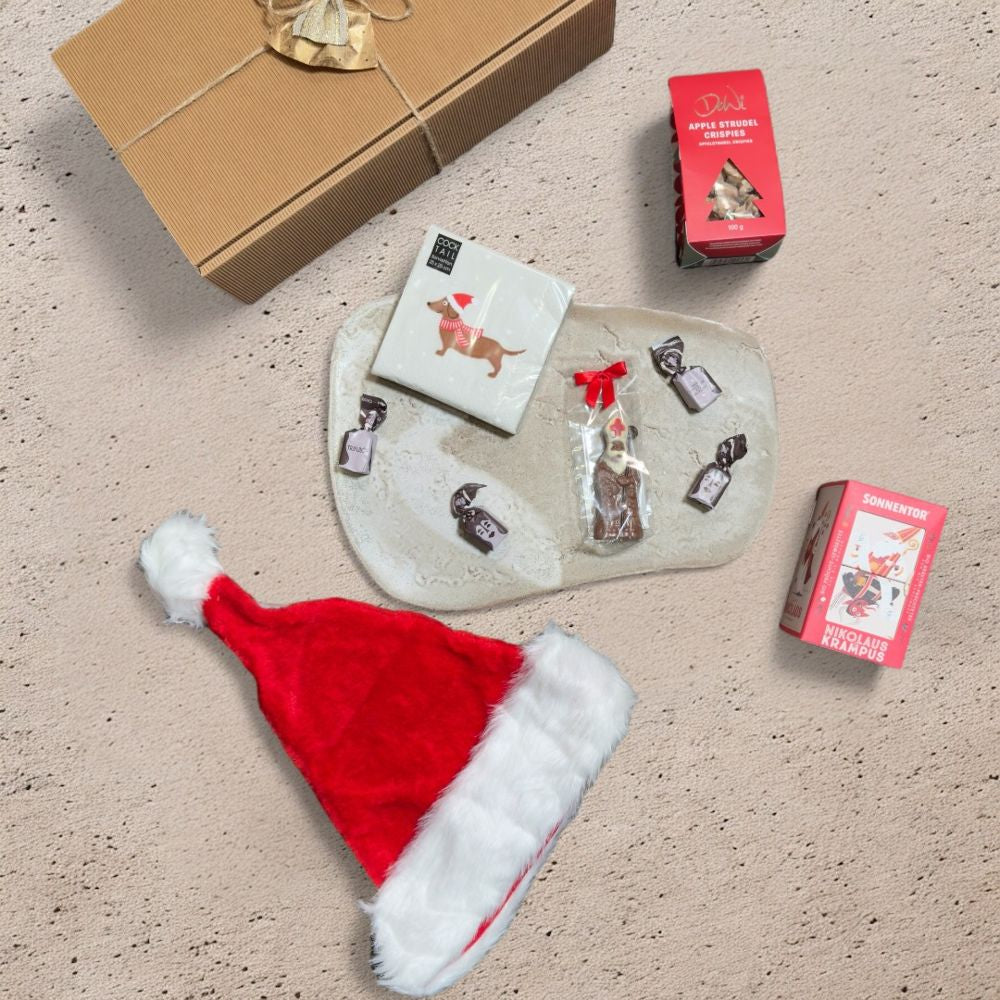 Ausgepacktes Nikolaus Geschenkset mit Sonnentor Nikolaus und Krampus Tee Süßwaren Albrecht Mini Bischof DeWi Apfelstrudel Crispies Tartufo schwarz Santa Mütze Samt Pelzimitat und Xmas Dackel Servietten